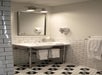 A bathroom with white subway tiles, a wall-mounted mirror, a sink with towels, a hairdryer, and a floor with black and white hexagonal tile pattern.