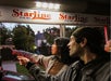 Two people point outside while standing near a StarLine Tours booth, with trees and a house visible in the background at dusk.
