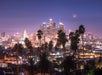 Los Angeles city skyline at dusk with illuminated buildings, palm trees in the foreground, and a crescent moon in the sky.