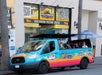 A colorful Hollywood Bus Tours van with passengers is parked outside the Hollywood Visitor Center on a sunny day.