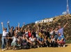 A large group of hikers wearing sunglasses posing for a group photo with the Hollywood sign in the background.