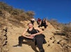 Several women in hiking clothes standing on different levels of a rocky path posing for a photo on a sunny day.