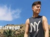 A man wearing a gray NY tank top looking to the right on a sunny day with the Hollywood sign in the background.