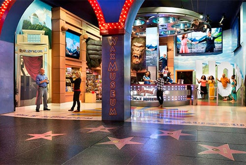 Entrance to a wax museum with large Hollywood-themed displays, staff at a reception desk, and star tiles on the floor resembling the Walk of Fame.