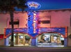 The Hollywood Wax Museum entrance at night, brightly lit with neon and marquee lights, featuring blue and red signage and visible displays inside.