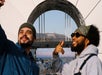 Two people pose for a selfie in front of an observation deck, with the Hollywood sign visible in the distant background.
