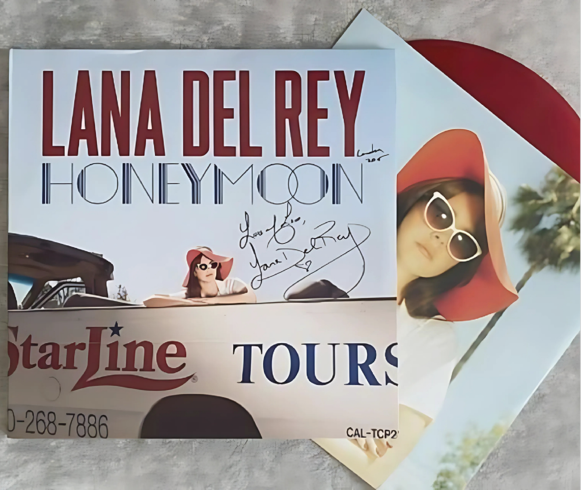 A signed Lana Del Rey "Honeymoon" vinyl album cover and record, featuring Lana Del Rey in sunglasses and a red hat next to a tour bus.