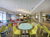 A modern, spacious lounge area with colorful chairs, round tables, and a large couch in an open, well-lit setting.