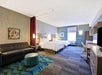 Spacious hotel room with two beds, a sofa, a round ottoman, desk, and modern decor. A large window provides natural light.