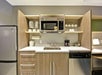 Kitchenette with a sink, microwave, dishwasher, mini-fridge, and open shelving holding dishes and glasses.