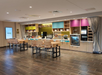A modern hotel breakfast area with high tables, wooden chairs, food displays, and signs reading "Inspired Table" and "Complimentary Breakfast.
