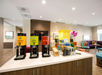 Coffee and beverage station with dispensers for gourmet, decaf, and hot water. Nearby, a seating area features colorful decor and furniture, including a yellow cabinet and potted orchid.