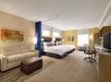 Two queen beds, sofa bed/seating area, desk and chair inside a guest room.