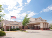 A two-story hotel building with an American flag in the front yard, under a partly cloudy sky.