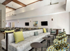 A modern lounge area with patterned chairs, a long sofa, round tables, and wall-mounted TVs. The room features high ceilings and ceiling fans.