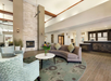 Lobby with modern decor featuring a curved sofa, armchair, round coffee table, white fireplace, and a reception desk.