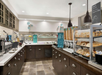 A self-service breakfast area with cereals, pastries, and various food items on display. Dark wood cabinets and a tiled floor complement the bright overhead lighting.