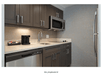 A kitchenette with dark brown cabinets, a small sink, dishwasher, coffee maker, microwave, and a refrigerator.