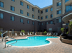 Outdoor pool surrounded by lounge chairs in a courtyard of a multi-story hotel building on a sunny day.