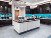 Modern buffet area with chafing dishes, beverage dispensers, and a central island. Blue tiled backsplash and dark cabinets enhance the decor.