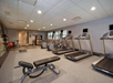 A gym with treadmills, an exercise bench, and fitness equipment. Carpeted floor and overhead lights illuminate the room.