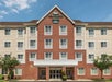 Front view of a four-story Homewood Suites by Hilton hotel with brick and beige siding, featuring a central entrance and a clear blue sky above.