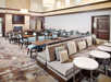 Hotel lounge with seating area, tables, and a fireplace. Neutral tones with modern decor.