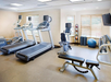 A gym with treadmills, an exercise bike, a bench, weights, a yoga ball, and wall-mounted TV in a brightly lit room.