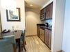 Compact hotel kitchenette with wooden cabinets, stainless steel appliances, a microwave, and a small dining area.