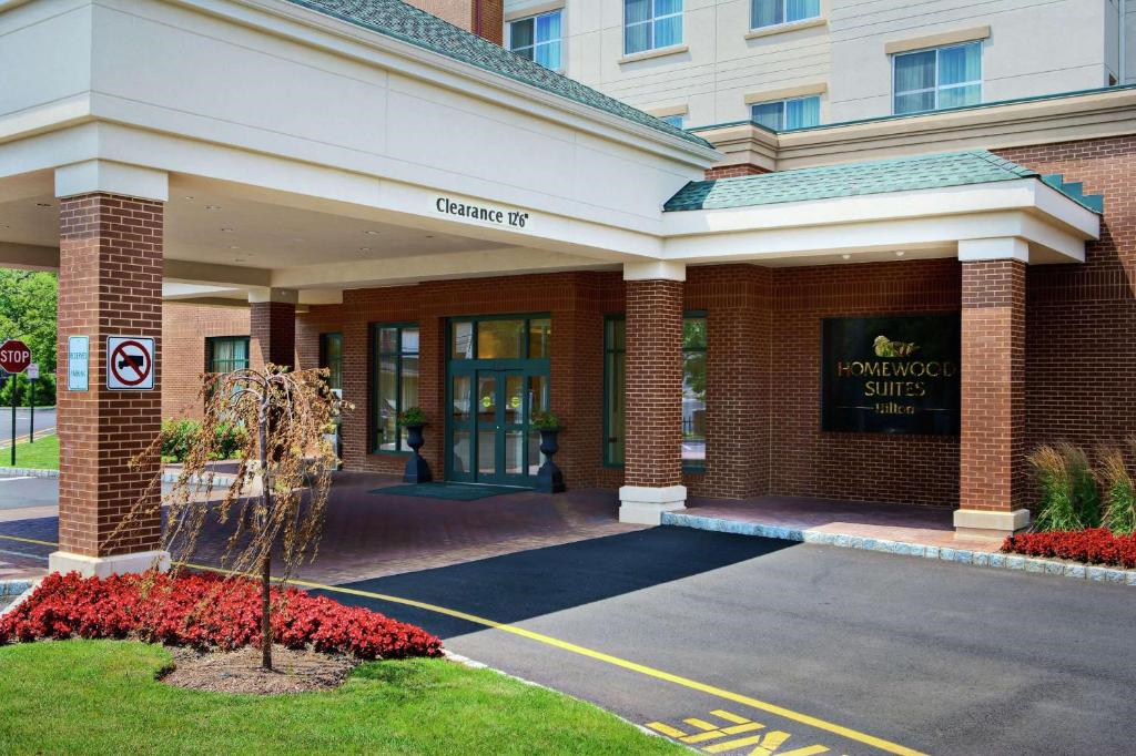 The entrance of a Homewood Suites hotel with a covered driveway, brick exterior, and landscaped plants near the main doors.