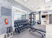 A gym with free weights, a bench, exercise mats, resistance bands, mirrors, a fire extinguisher, and a digital clock on the wall.