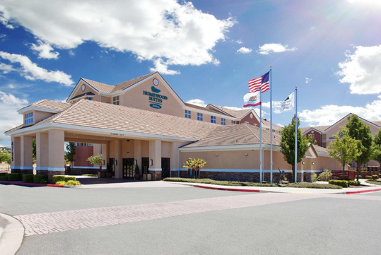 Hotel exterior with a light beige facade, multiple flags, and a clear blue sky in the background.