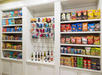 Shelves stocked with assorted snacks, beverages, chips, candy, and toiletries in a white cabinet display.
