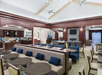 Hotel lobby with modern decor, including brown tables, gray seating, and a breakfast area. A TV is mounted on a wood-paneled wall. Ceiling fans and large windows provide a spacious feel.