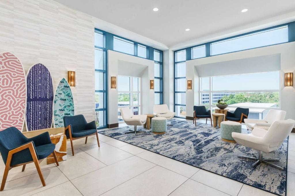 Modern lounge area with blue and white chairs, small tables, surfboard wall art, large windows, and a blue patterned rug.
