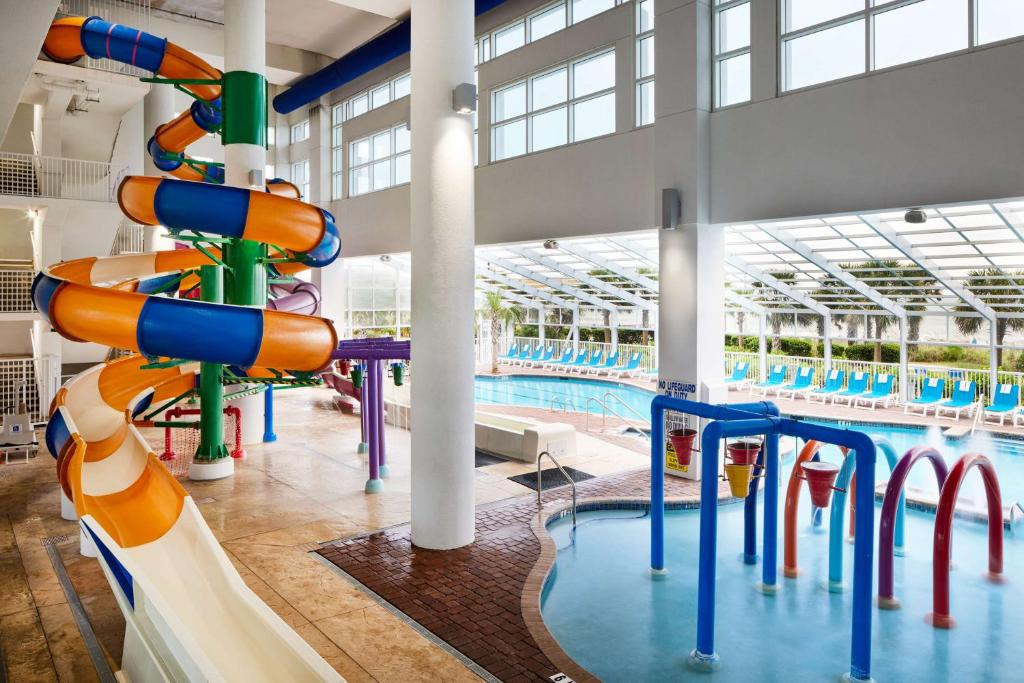 Indoor aquatic center with a twisty water slide, splash play area, and large lap pool, surrounded by lounge chairs and large windows.