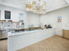 A clean, modern ice cream shop interior with a white counter, glass display case, menu boards, and two checkout registers under gold pendant lights.