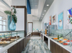 Modern buffet area with various food options displayed on counters, glass partitions, decorative vase, and framed artwork on the walls.