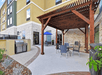 A concrete patio with a dark wooden gazebo over a table and chair with another table in the background at the Homewood Suites by Hilton New Braunfels.