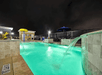 An outdoor pool with the water lit up at night and several small water falls flowing into it and chairs lining the sides at night.