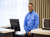 A desk clerk in a blue shirt standing in front of a computer behind the desk at the Homewood Suites by Hilton New Braunfels.