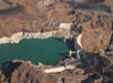Aerial view of Hoover Dam spanning a turquoise reservoir in a rocky desert landscape, with roads and infrastructure visible around the dam.