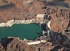 Aerial view of a large dam holding back turquoise water, surrounded by rocky, arid terrain with winding roads.