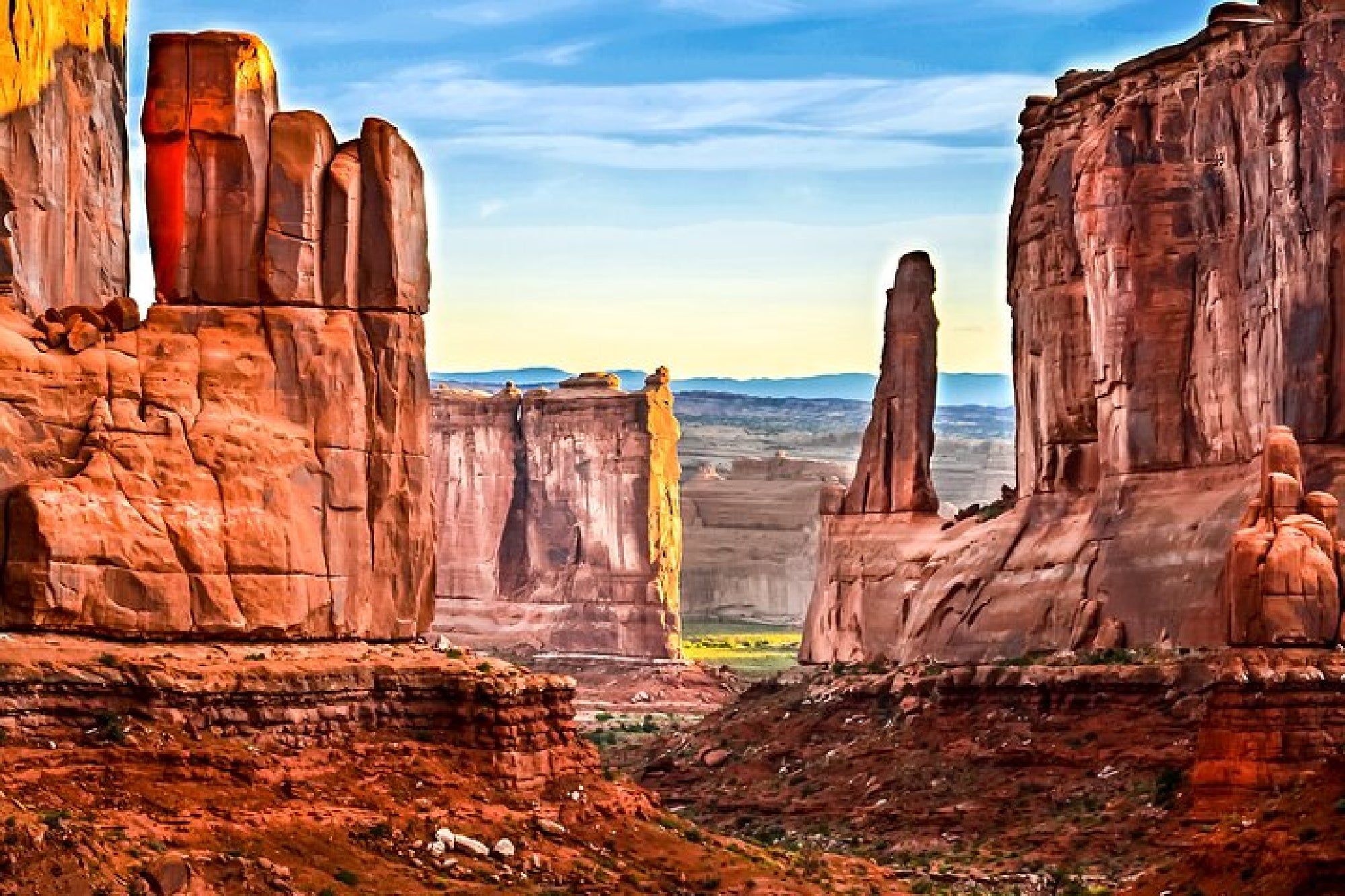 Red rock formations and cliffs under a blue sky in a desert landscape, likely in a national park in the American Southwest.