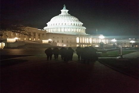 A group of people walk toward the illuminated United States Capitol building at night.