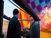 A hot air balloon pilot dressed in all black aiming a gun shooting fire into the balloon to fill it with hot air.