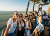 A group of young women wearing sun glasses posing for a photo while in the air in a hot air balloon on a sunny day.