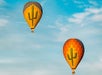 Two yellow hot air balloons with green cacti on them high in the air with a light blue clouded sky behind them.
