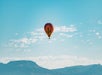 A single multicolored hot air balloon with a cactus on it in the wait with a bright blue sky behind it on a sunny day.