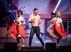 Two women in big pink skits dancing on either side of a man holding a guitar at Hot Rods & High Heels in Branson, Missouri.
